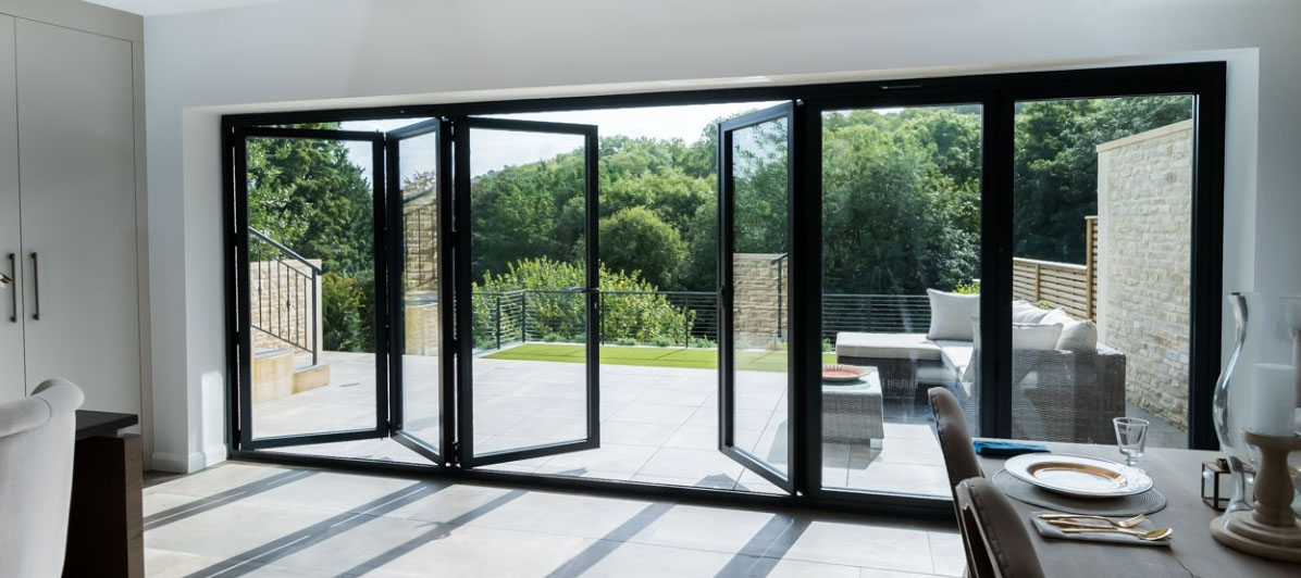 Wide black aluminium folding glass doors opening to a lush green garden