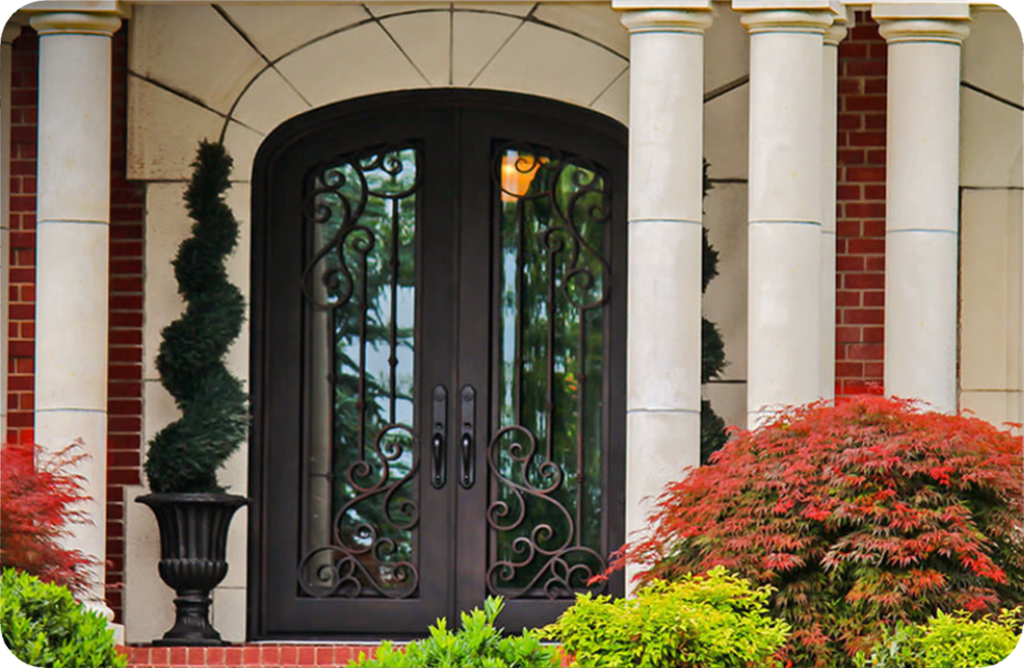 Elegant black wrought-iron front entry door with glass panels framed by stone columns and landscaping at a modern home exterior